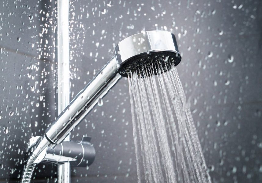 Fresh shower behind wet glass window with water drops splashing. Water running from shower head and faucet in modern bathroom.